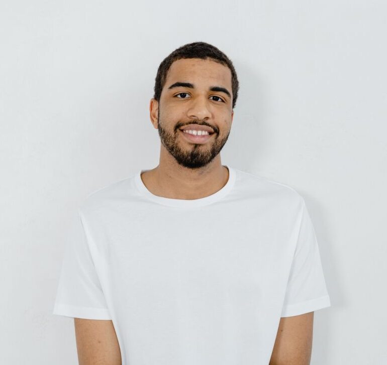 Casual portrait of a smiling man in a minimalist white t-shirt with copy space on a plain background.